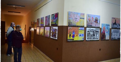 Zwiedzanie wystawy poplenerowej - obraz uczestników pleneru wiszą na ścianie, obok dwójka uczestników wystawy